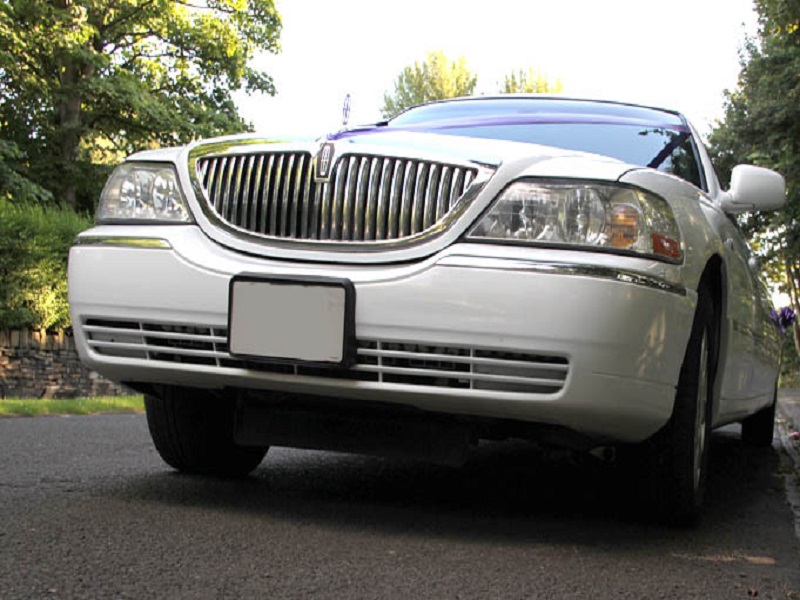 A professional chauffeur opening the door of a white Lincoln Stretch limousine in Redbridge.
